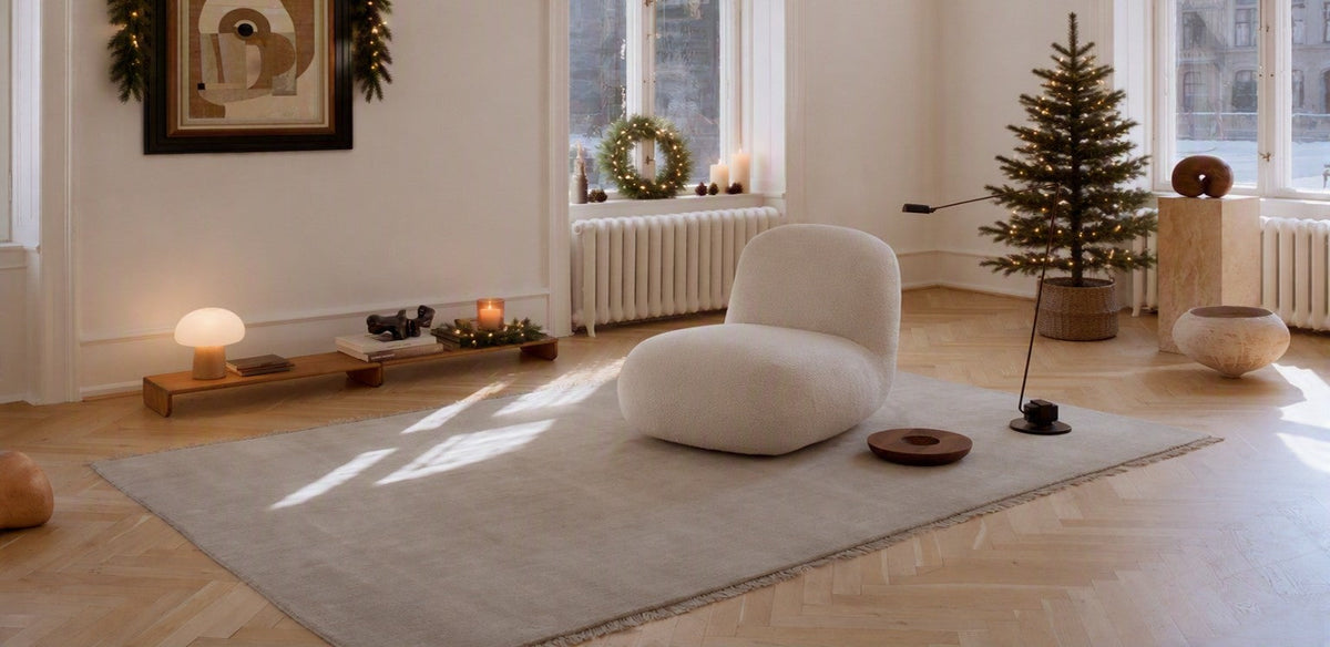 A warmly lit living area with minimalist feel at Christmas with beautiful large floor rug and statement boucle lounge chair